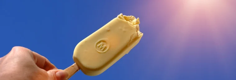 Magnum ice cream bar held against a blue sky near the sun.