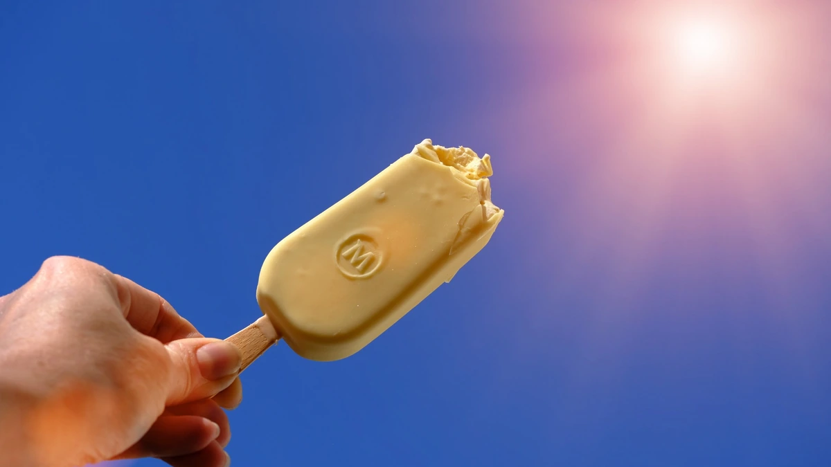 Magnum ice cream bar held against a blue sky near the sun.