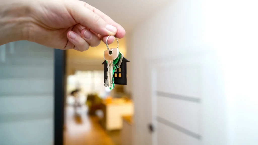 A hand holding house keys inside a modern apartment.