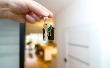 A hand holding house keys inside a modern apartment.