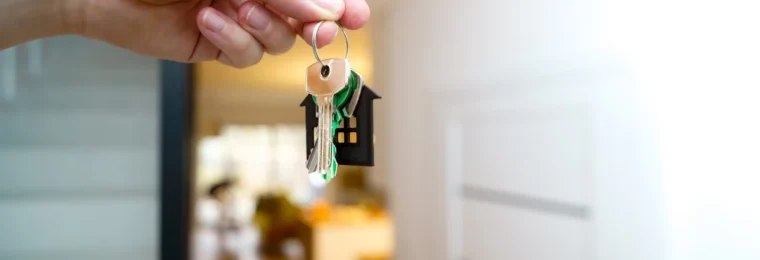 A hand holding house keys inside a modern apartment.