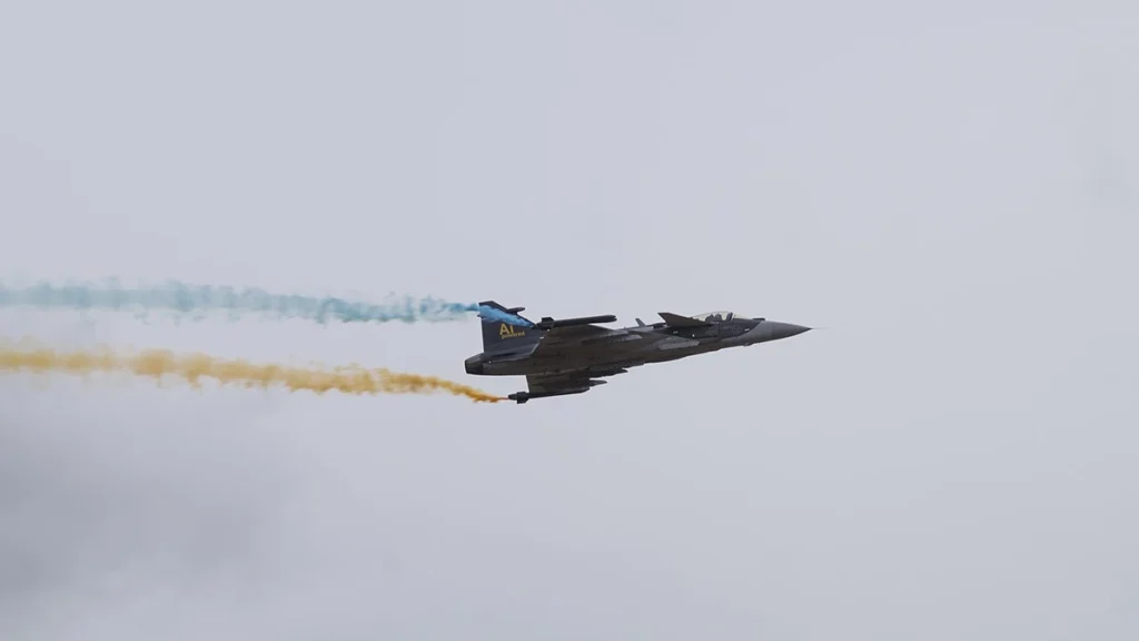 Gripen E 39-6002 flying during Flygdagarna 2026 in Malmen, Linköping, trailing blue and yellow smoke.