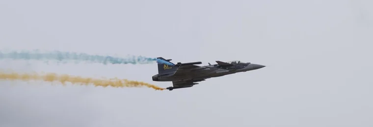 Gripen E 39-6002 flying during Flygdagarna 2026 in Malmen, Linköping, trailing blue and yellow smoke.
