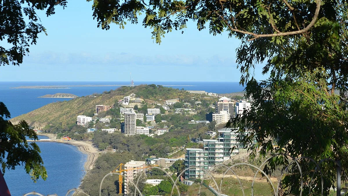 View of Port Moresby, Papua New Guinea, with coastline, hillside buildings and foreground tree branches.