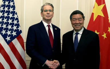 U.S. Treasury Secretary Scott Bessent and Chinese Vice Premier He Lifeng shake hands between U.S. and Chinese flags during trade talks in Geneva in May 2025.