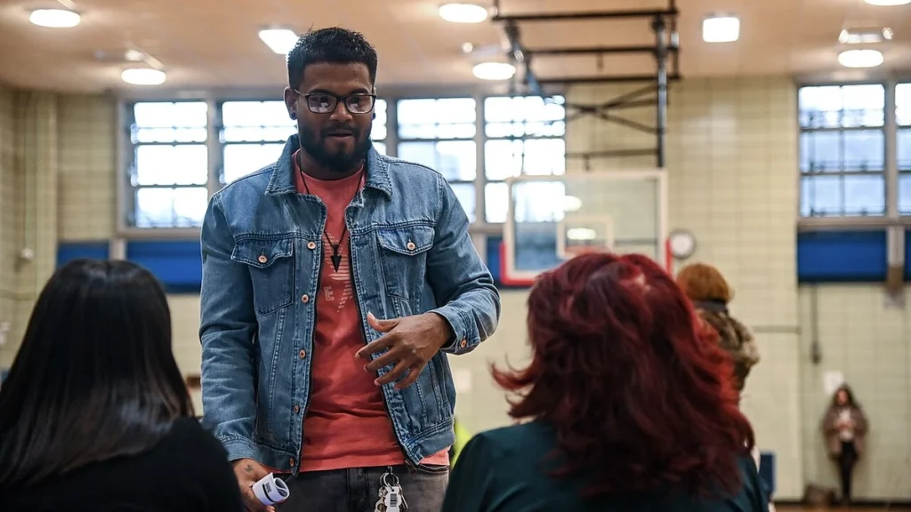 A man speaks with attendees seated at a table during an MTA job fair in East Harlem, New York.