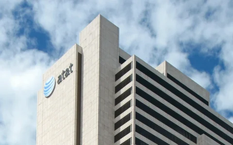 Upper floors of AT&T's Whitacre Tower in Dallas, with the blue AT&T logo and lettering visible against a cloudy sky.