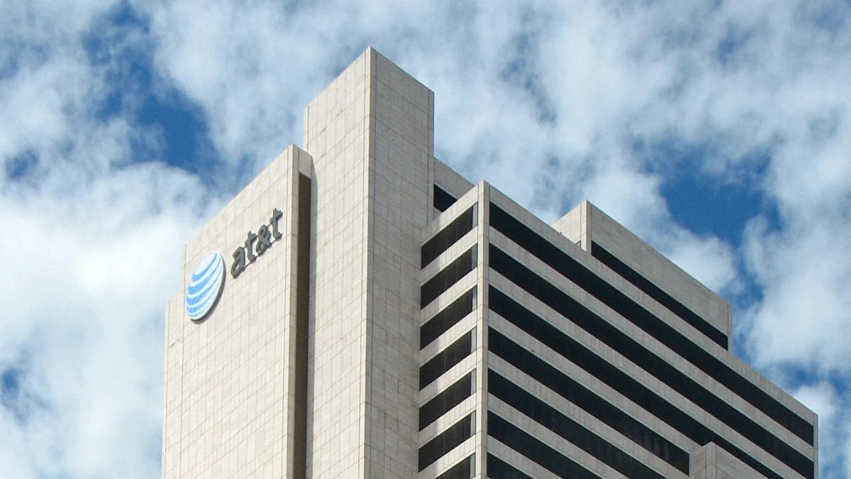 Upper floors of AT&T's Whitacre Tower in Dallas, with the blue AT&T logo and lettering visible against a cloudy sky.