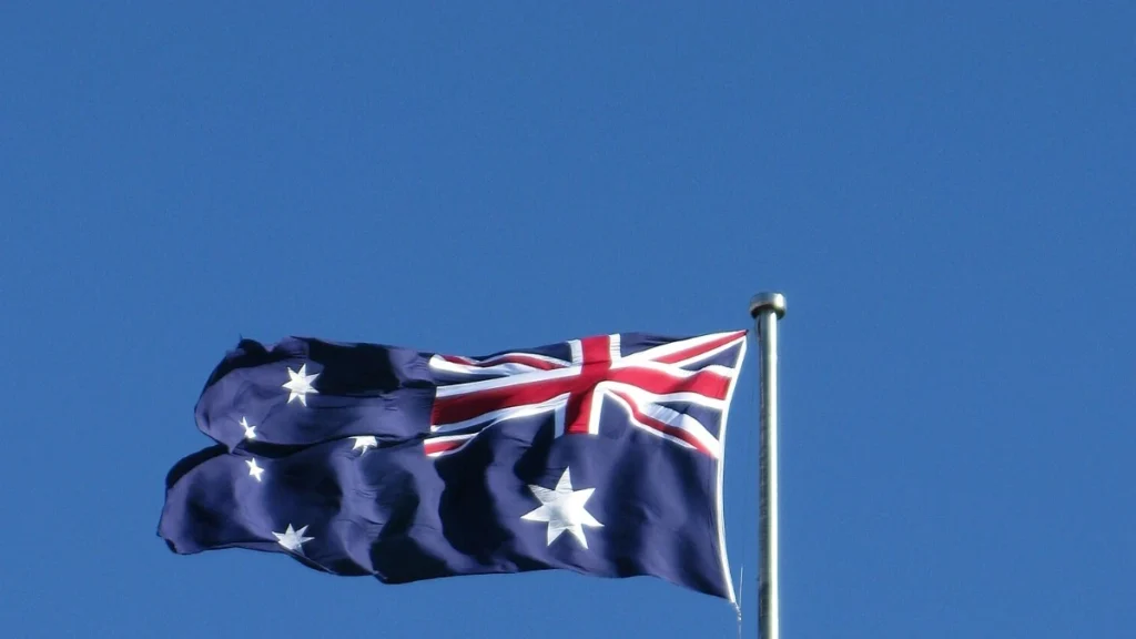 Australian flag flying on a flagpole against a blue sky.