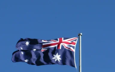 Australian flag flying on a flagpole against a blue sky.