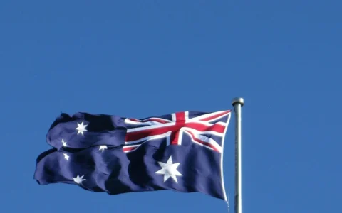 Australian flag flying on a flagpole against a blue sky.