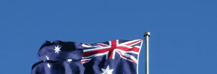 Australian flag flying on a flagpole against a blue sky.