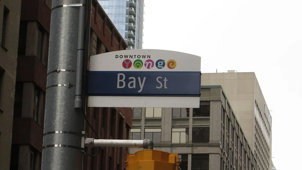 Bay Street street sign in Toronto's financial district, with buildings and a traffic signal in the background.