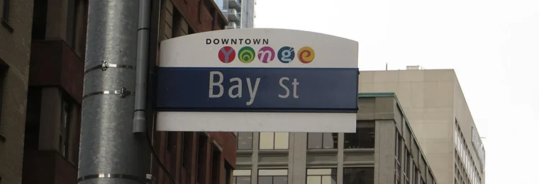 Bay Street street sign in Toronto's financial district, with buildings and a traffic signal in the background.