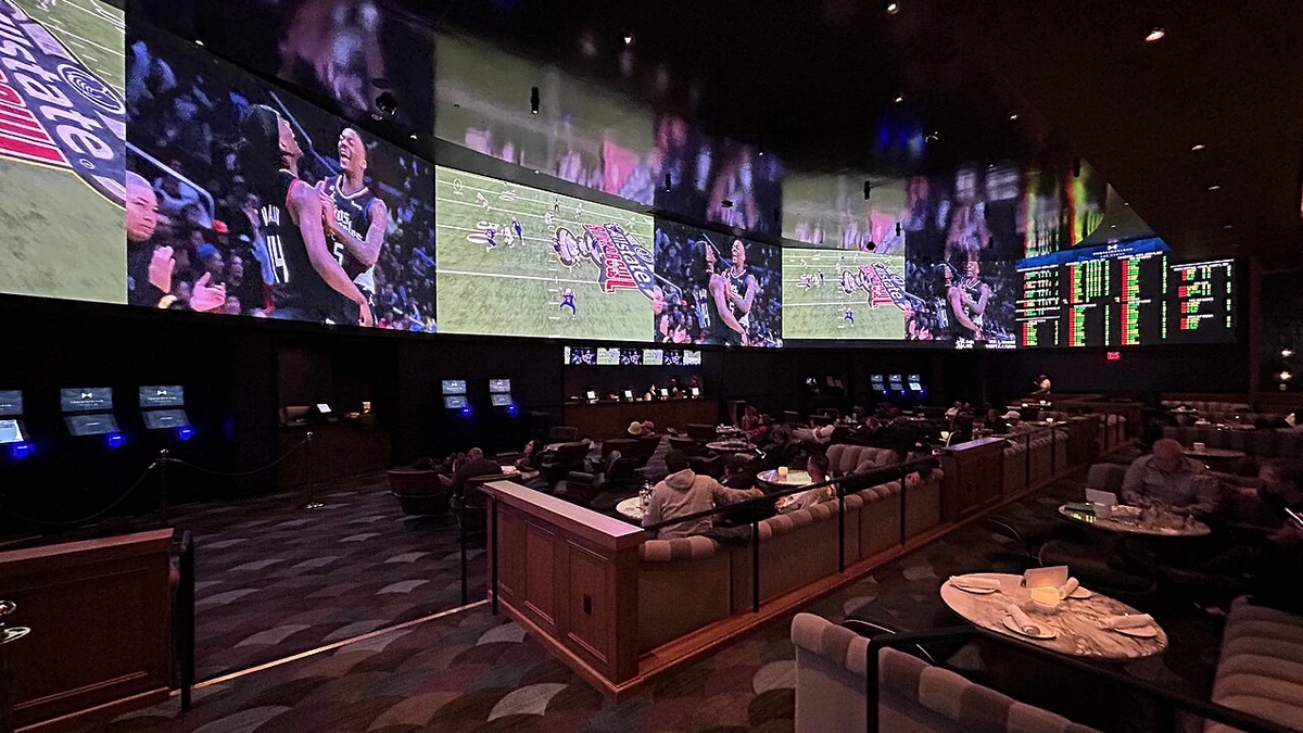 Sportsbook interior at Fontainebleau Las Vegas with large sports screens, betting odds boards and customer seating.