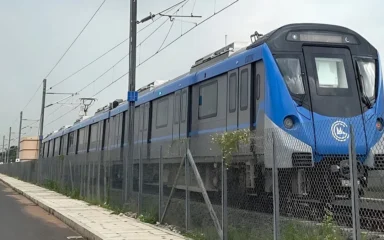 Blue Chennai Metro Phase 2 trainset at Poonamallee depot, viewed behind a fence.