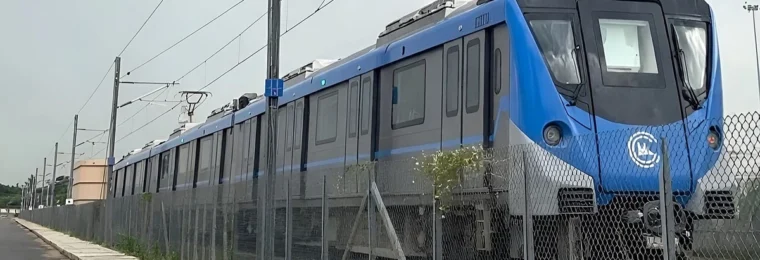 Blue Chennai Metro Phase 2 trainset at Poonamallee depot, viewed behind a fence.