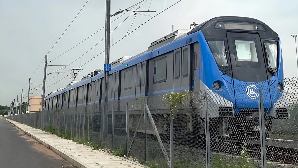 Blue Chennai Metro Phase 2 trainset at Poonamallee depot, viewed behind a fence.