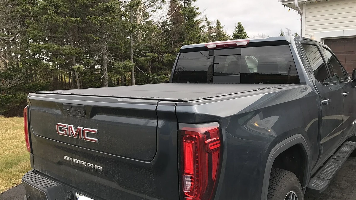 Rear three-quarter view of a dark gray GMC Sierra pickup truck fitted with a low-profile tonneau cover over the truck bed.