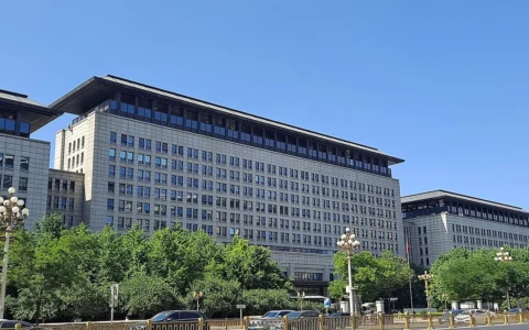 Exterior of China’s Ministry of Commerce building, with trees and vehicles along the street.