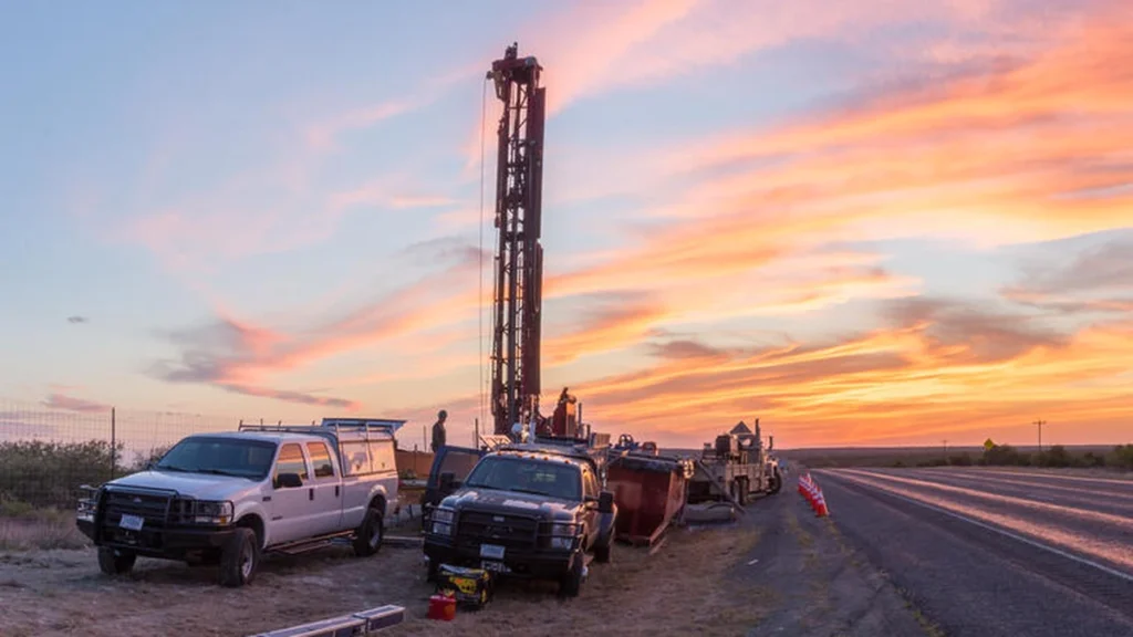 A USGS research drilling rig and service trucks beside a Texas highway at dawn near Brackettville.