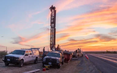 A USGS research drilling rig and service trucks beside a Texas highway at dawn near Brackettville.