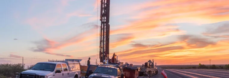 A USGS research drilling rig and service trucks beside a Texas highway at dawn near Brackettville.