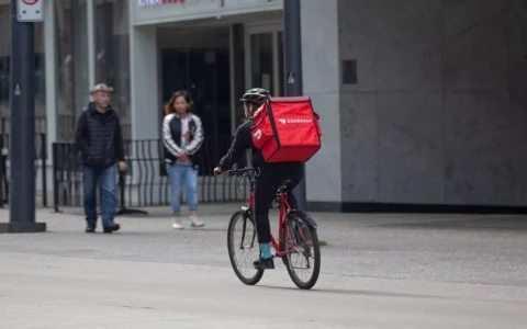 DoorDash bicycle courier riding along a city street with a red DoorDash delivery bag.