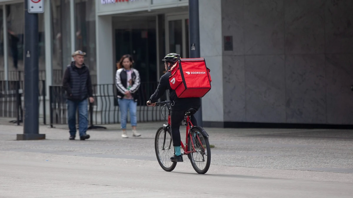 DoorDash bicycle courier riding along a city street with a red DoorDash delivery bag.