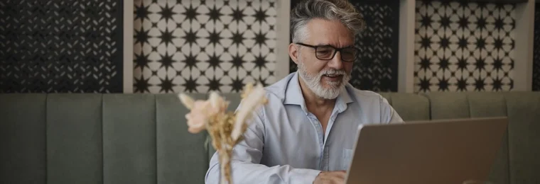 An older man with gray hair and glasses using a laptop at a cafe table.