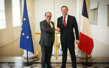 Emmanuel Moulin, left, shaking hands with Christophe Hansen between European Union and French flags in Paris.