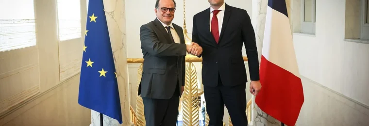Emmanuel Moulin, left, shaking hands with Christophe Hansen between European Union and French flags in Paris.