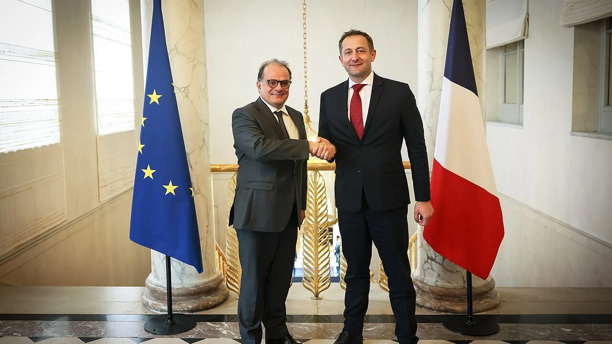 Emmanuel Moulin, left, shaking hands with Christophe Hansen between European Union and French flags in Paris.