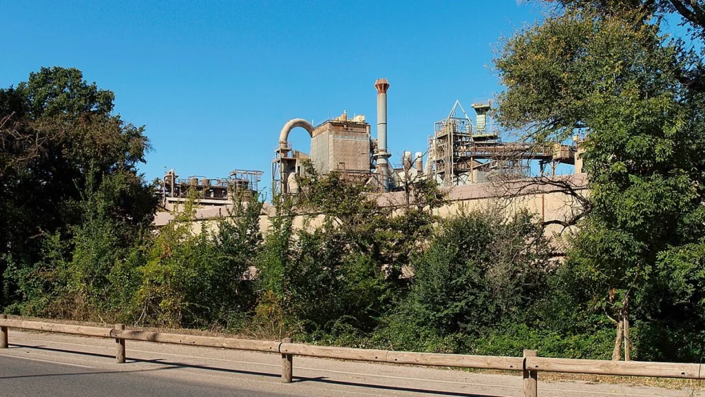 Alumina factory in Gardanne, France, seen behind trees from a roadside.
