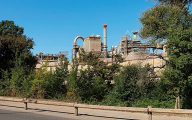 Alumina factory in Gardanne, France, seen behind trees from a roadside.