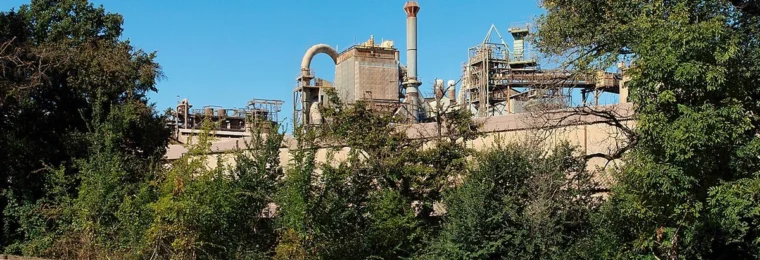 Alumina factory in Gardanne, France, seen behind trees from a roadside.