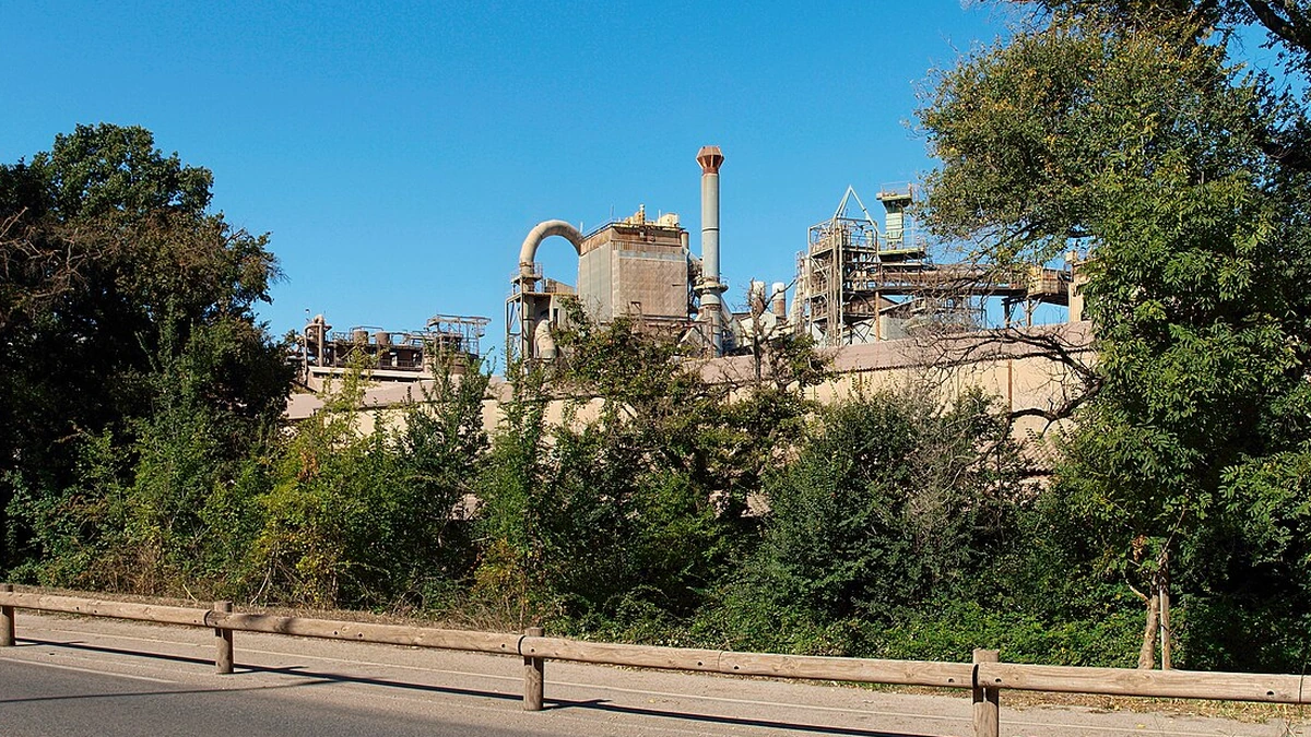 Alumina factory in Gardanne, France, seen behind trees from a roadside.