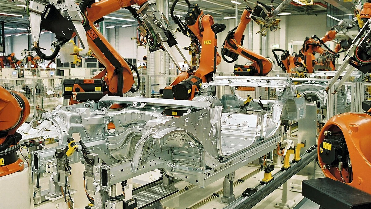 Orange industrial robots working on silver car bodies inside the BMW manufacturing plant in Leipzig, Germany.
