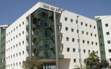 Exterior of the Israel Central Bureau of Statistics building in Jerusalem, with a glass-fronted entrance and Hebrew signage.