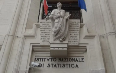 Entrance of the Istituto Nazionale di Statistica building in Rome with the Istat signage visible below a statue and Italian and European Union flags.