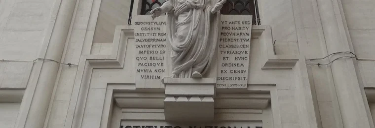 Entrance of the Istituto Nazionale di Statistica building in Rome with the Istat signage visible below a statue and Italian and European Union flags.