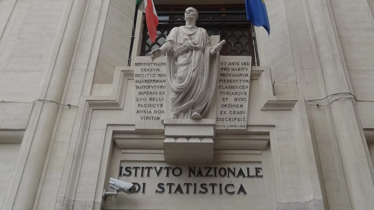 Entrance of the Istituto Nazionale di Statistica building in Rome with the Istat signage visible below a statue and Italian and European Union flags.