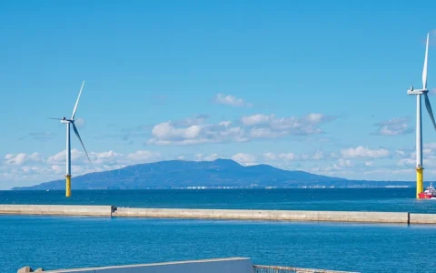 Two offshore wind turbines at Akita Port in Japan, with the Oga Peninsula across the water.