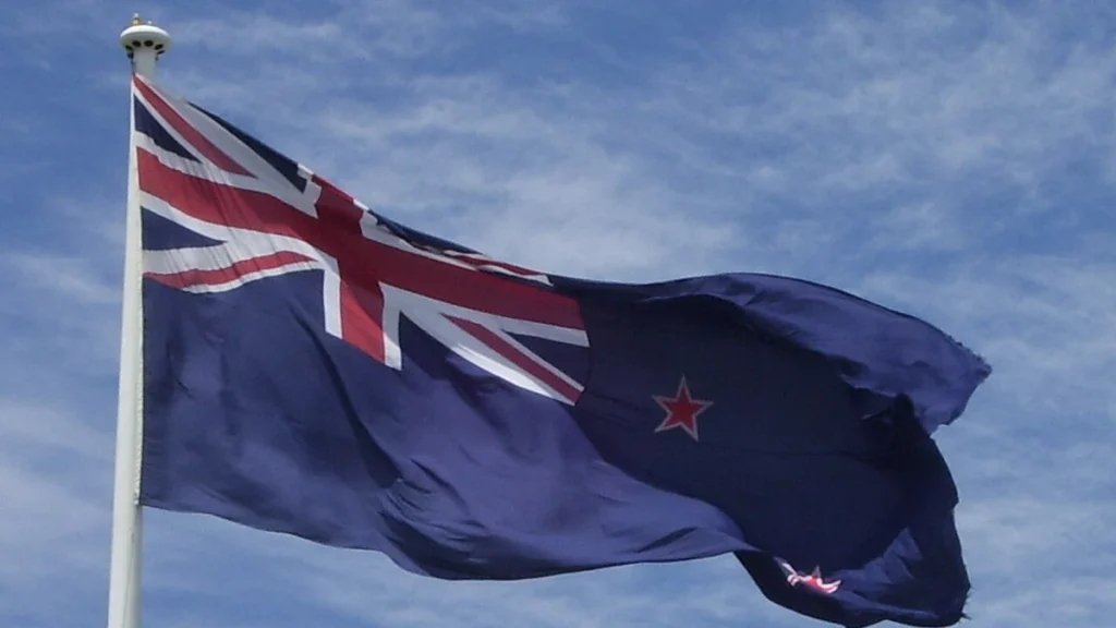 New Zealand flag flying at Auckland Airport against a blue sky.