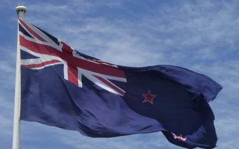 New Zealand flag flying at Auckland Airport against a blue sky.