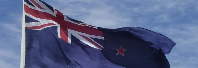New Zealand flag flying at Auckland Airport against a blue sky.