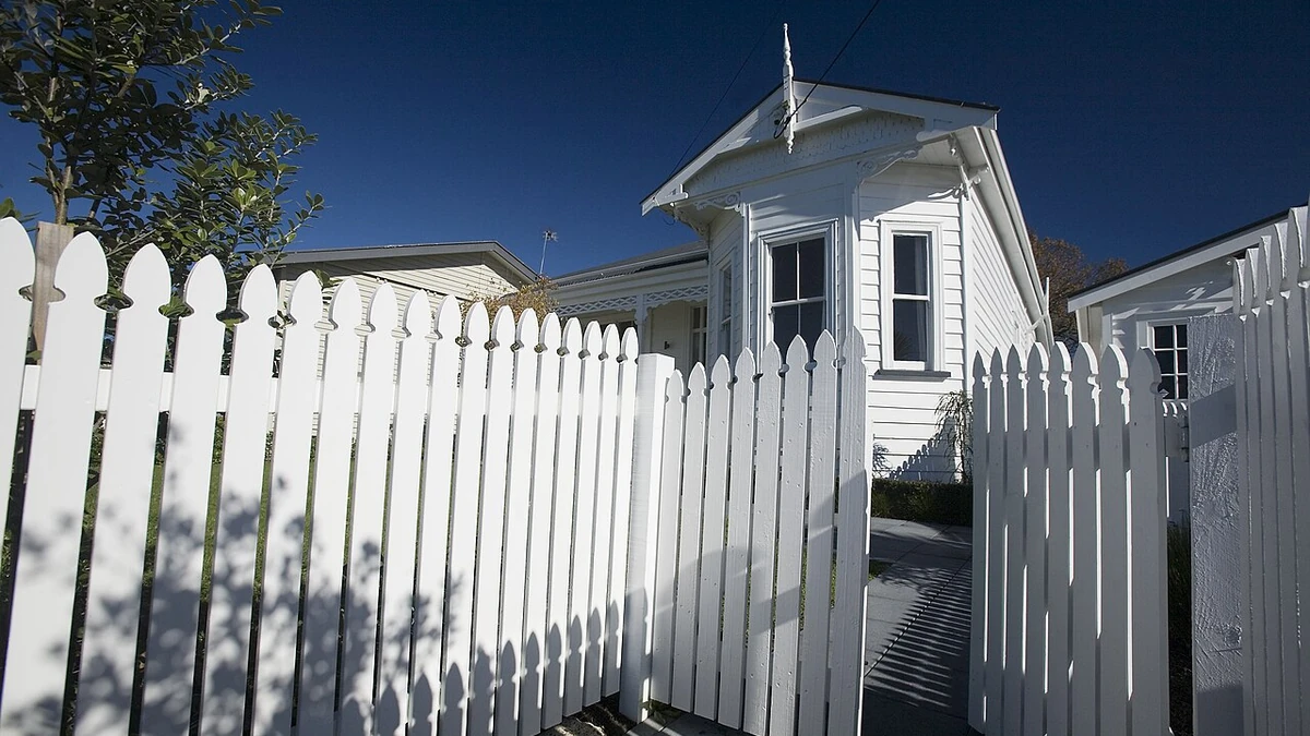 A white wooden house with a picket fence in Northcote Point, Auckland, under a blue sky.