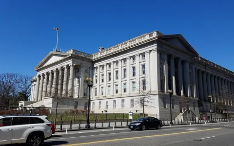 Exterior of the U.S. Treasury Building in Washington, D.C., seen from the street under a clear blue sky.