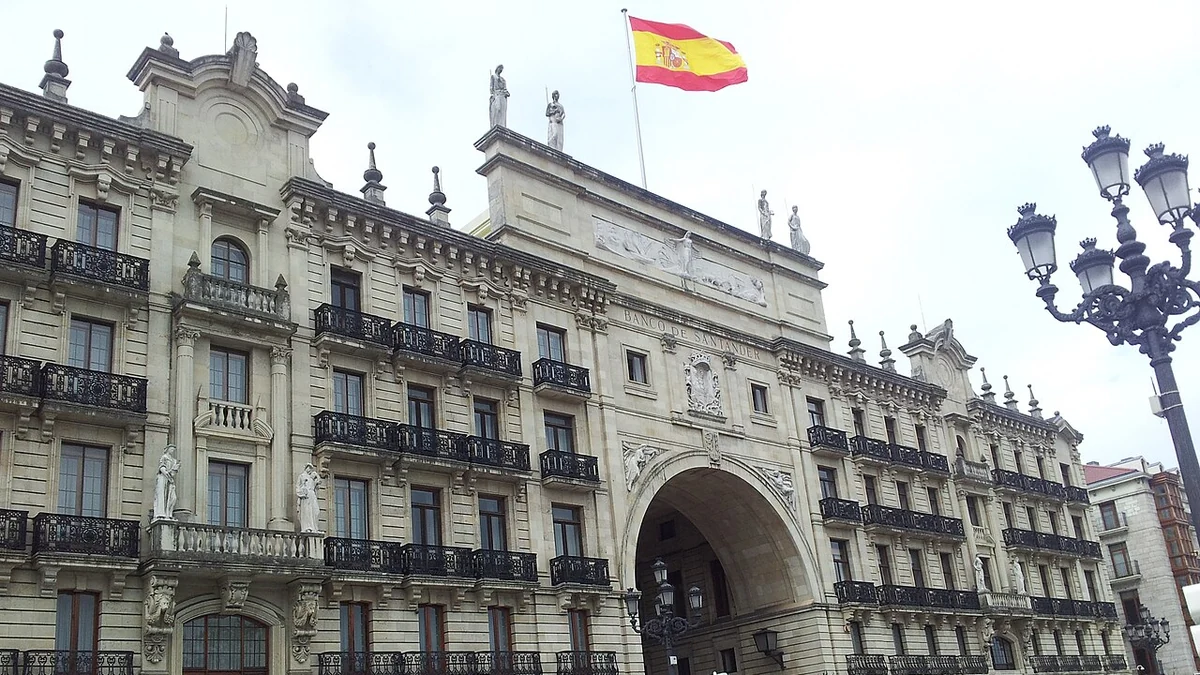 Stone facade of a Banco Santander building in Santander, Spain, with a Spanish flag flying over the central arch.