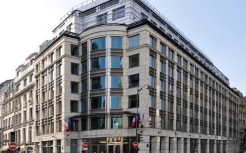 Exterior of the French financial regulator AMF headquarters at 17 Place de la Bourse in Paris, with French and EU flags outside.